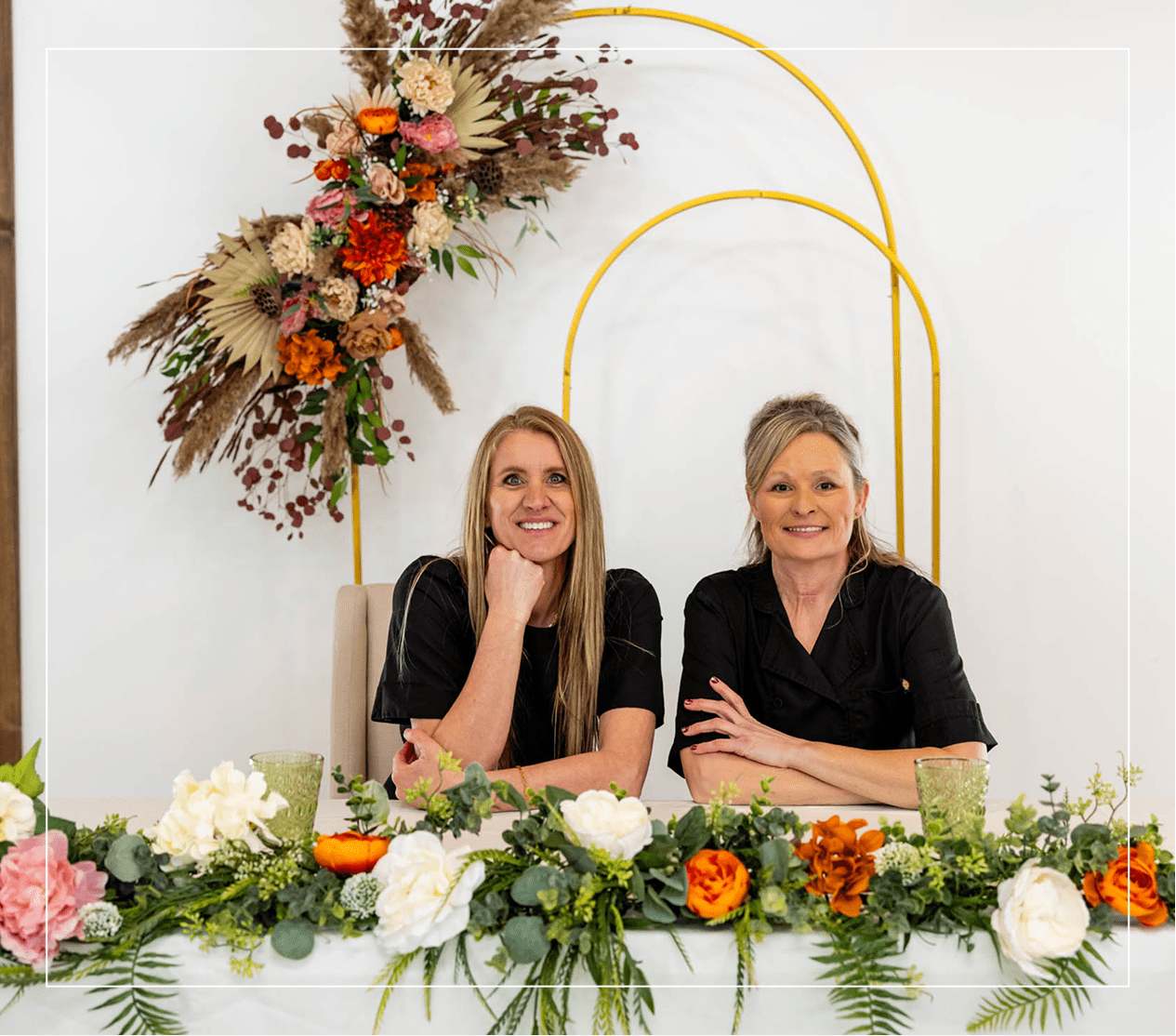 img2 (1) Two women sitting at a table with flowers.